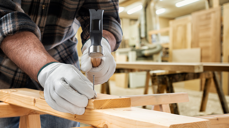 In een atelier heeft een man een hamer vast. Hij staat op het punt een nagel in hout te kloppen. Op de achtergrond staan deuren.