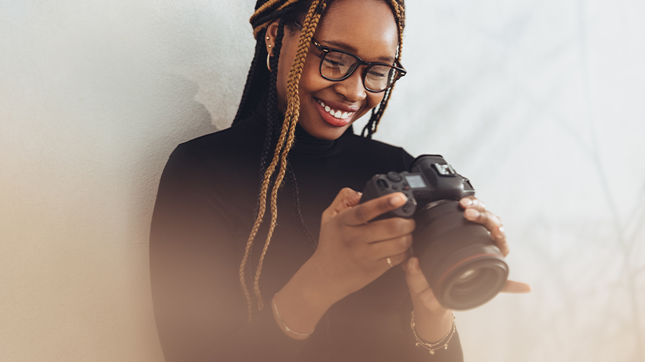 Een jonge vrouw kijkt lachend naar de camera in haar handen. Het is een reflexcamera met een grote lens. De vrouw houdt van fotografie en multimedia.